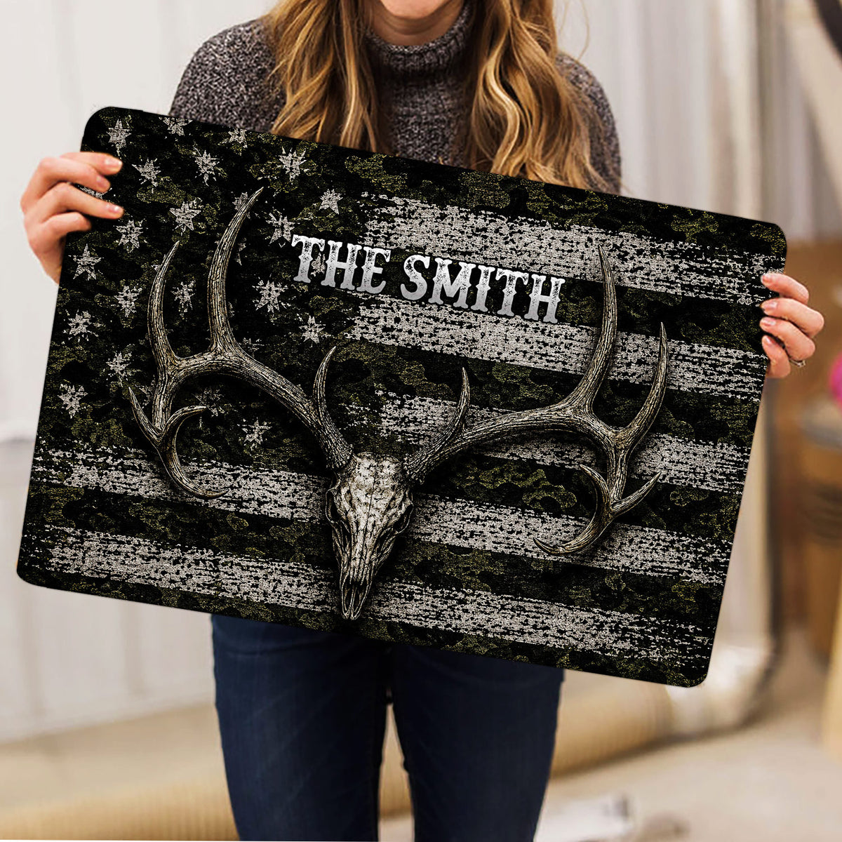Person holding a hunting doormat featuring a deer skull, antlers, camouflage and star details
