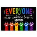 Black LGBT doormat with colorful rainbow lettering, inclusive welcome message, heart accents, and paw prints