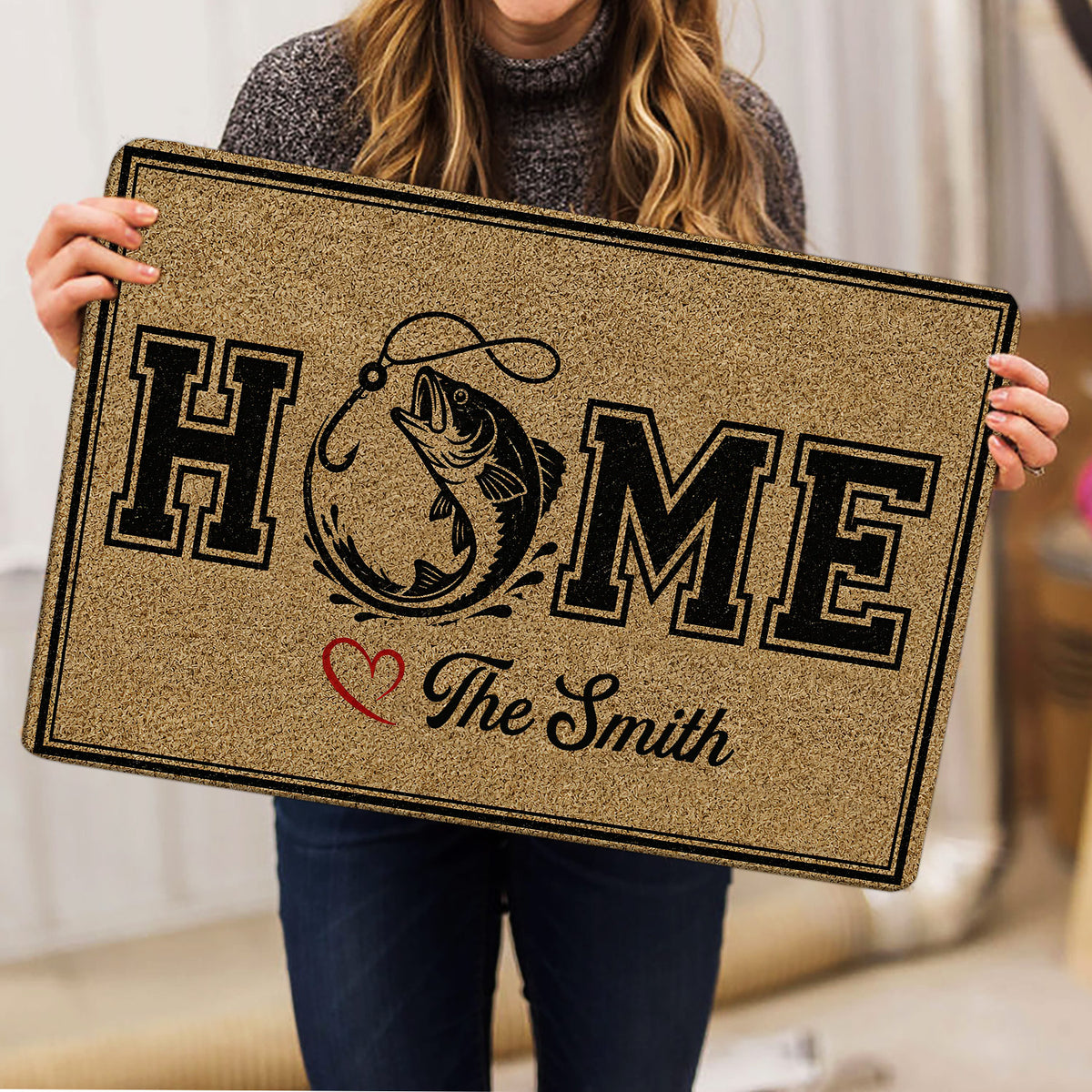 Person holding a fishing-themed doormat with a leaping fish illustration, bold lettering, and heart accent