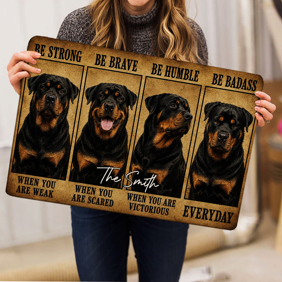 Person holding a Rottweiler doormat featuring four illustrated dogs and bold motivational artwork
