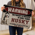 Person holding a distressed red, black, and cream Husky doormat indoors