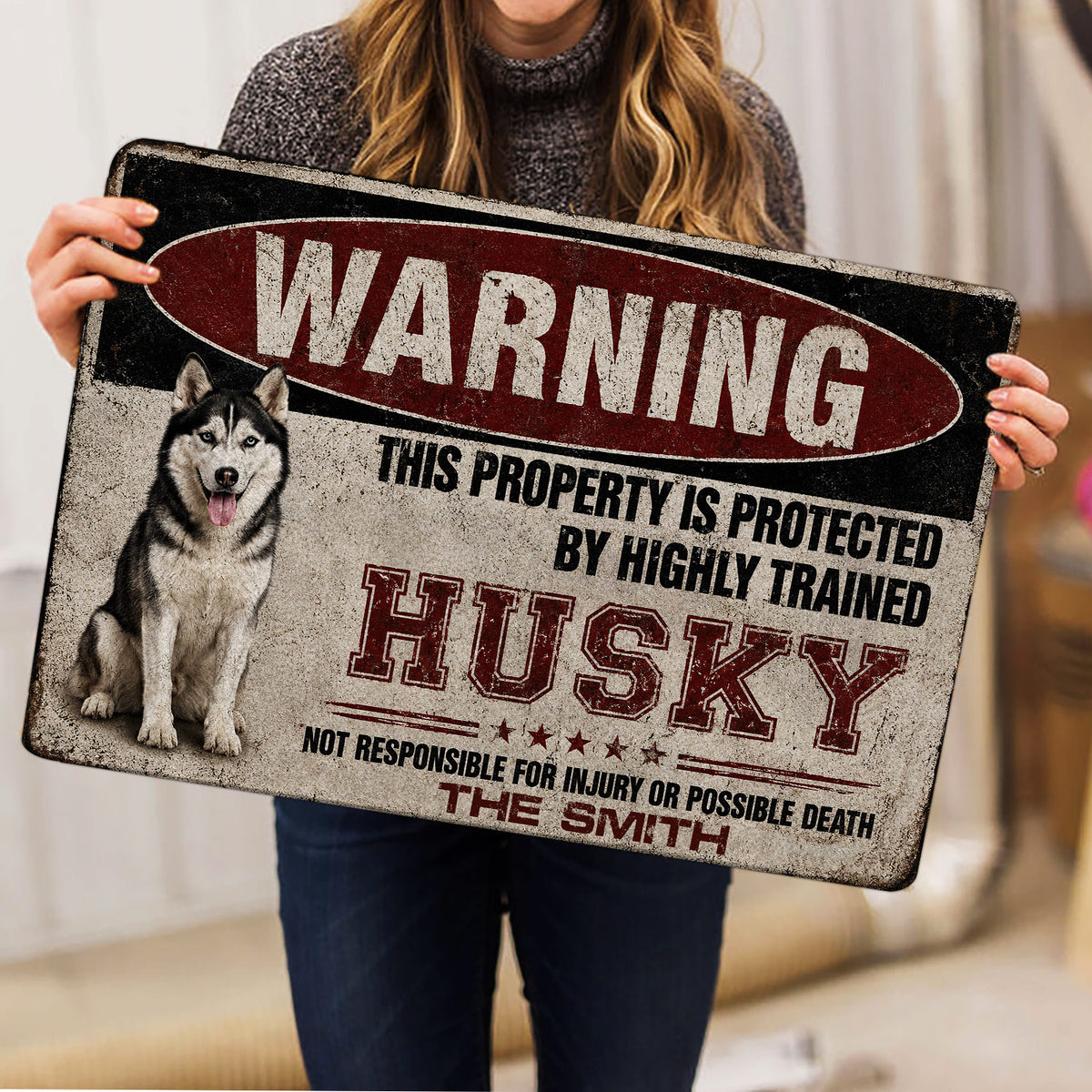 Person holding a distressed red, black, and cream Husky doormat indoors