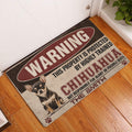 Chihuahua warning design doormat displayed beside a white door on a warm wood floor