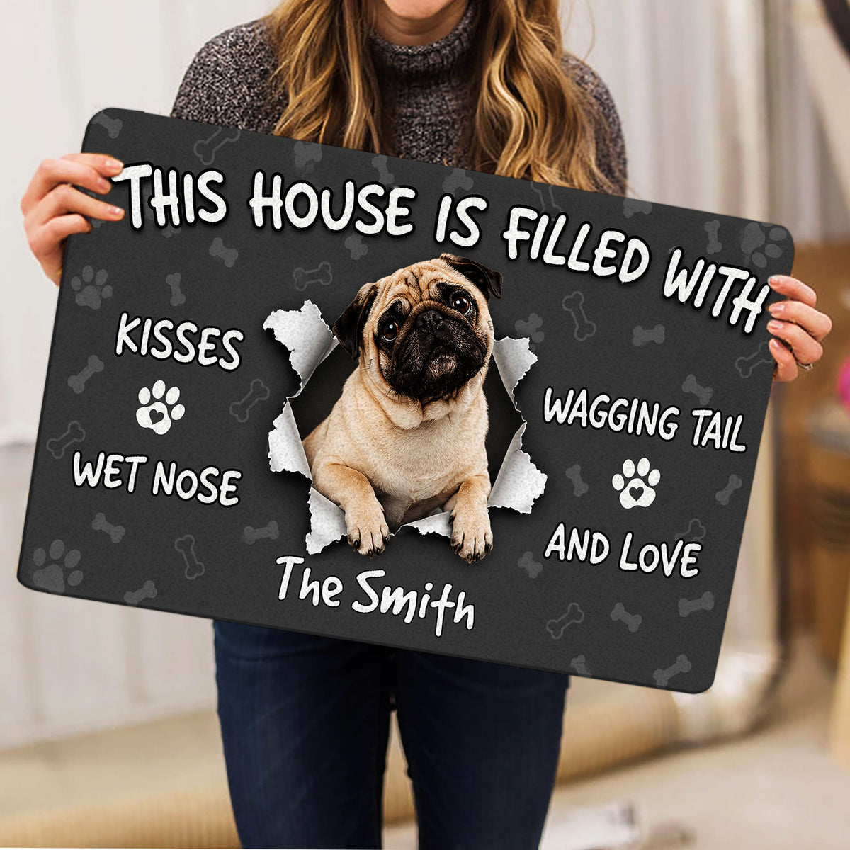 Person holding a pug doormat with a central pug illustration and playful dog-themed lettering
