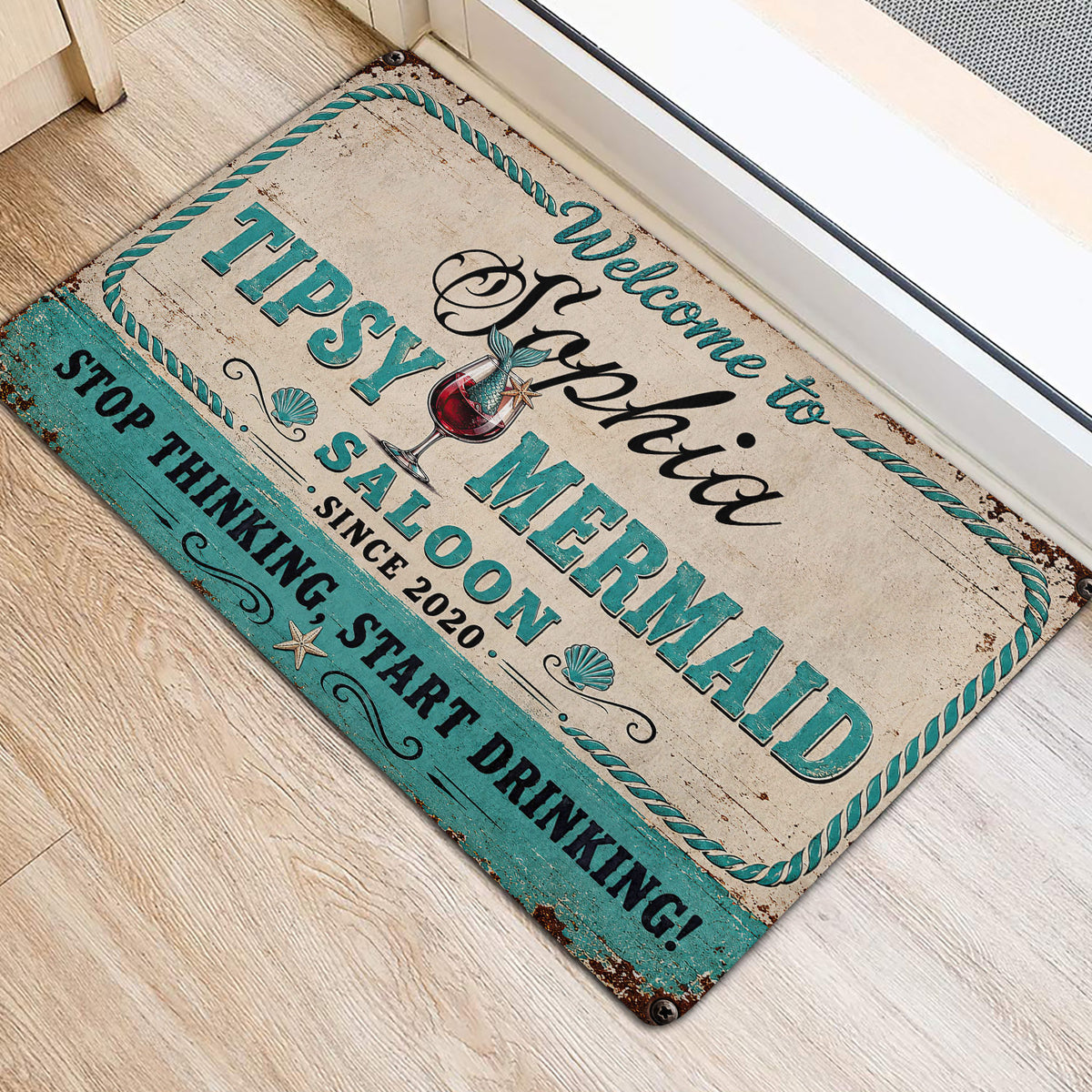 Turquoise and cream mermaid door mat displayed beside a bright entryway on light flooring