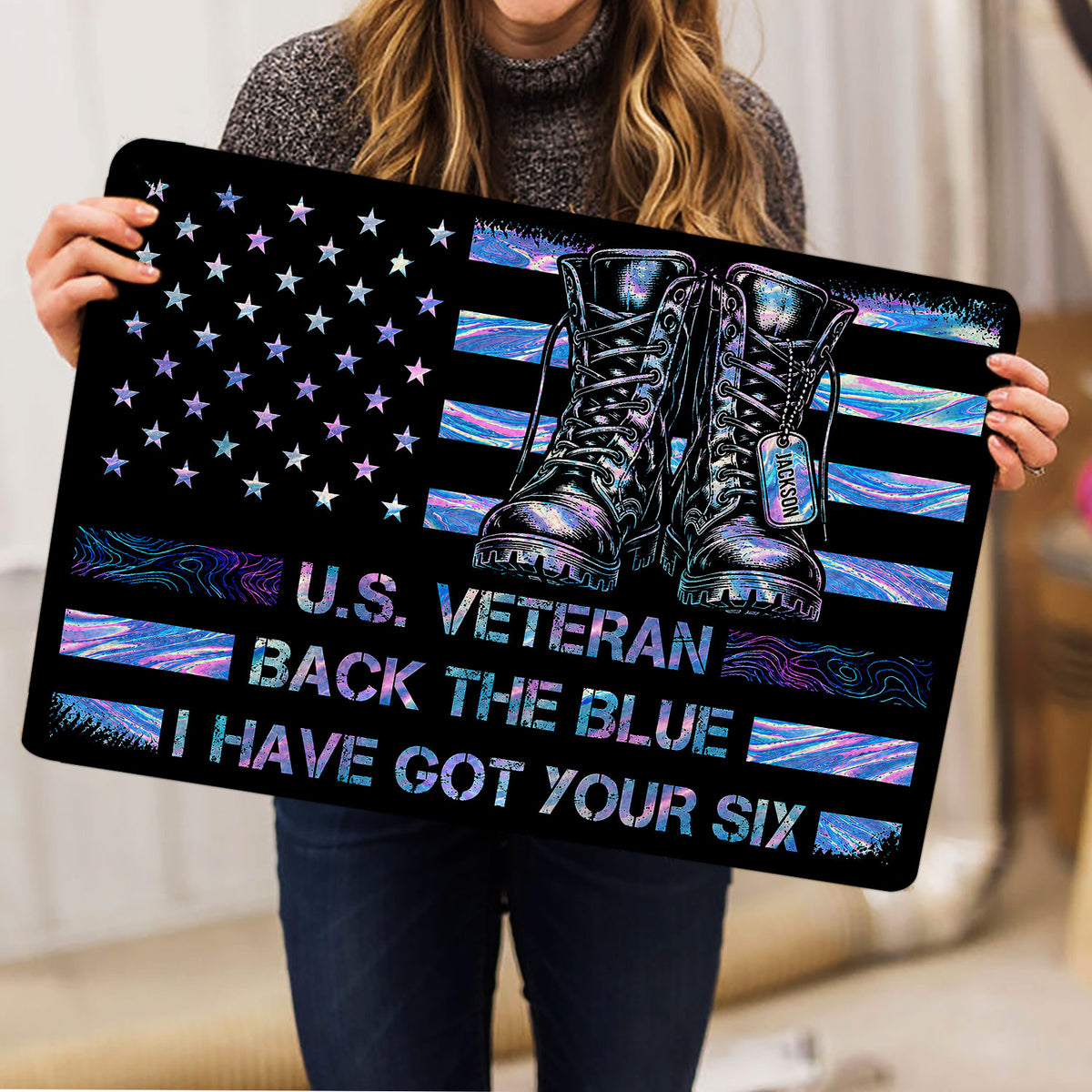 Person holding a veteran doormat featuring military boots, stars, and vibrant flag-inspired artwork