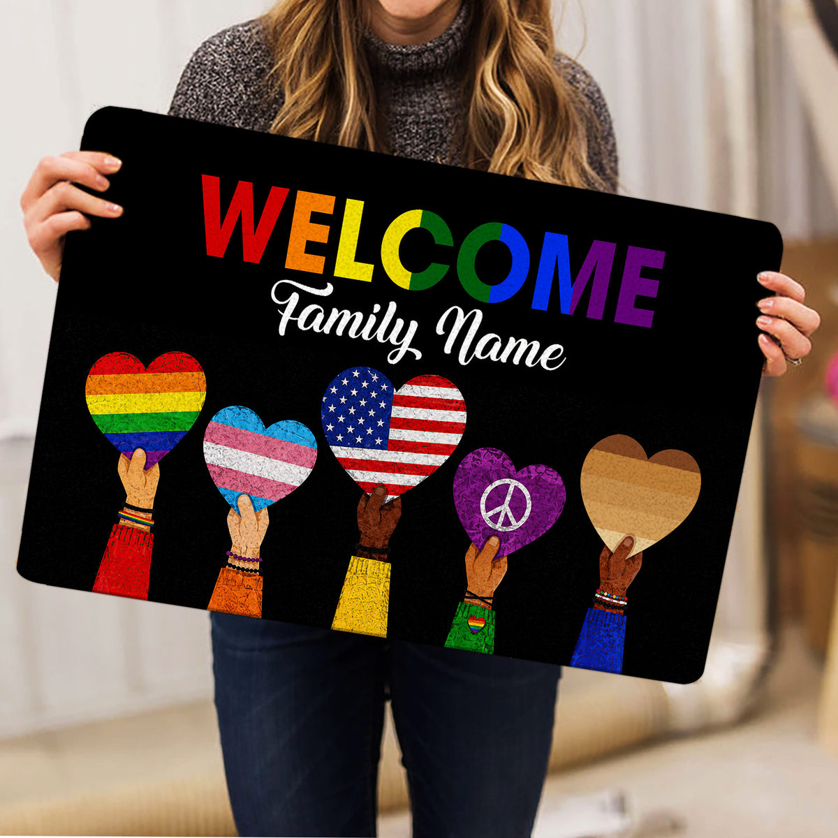 Person holding a black LGBT welcome doormat featuring pride hearts and vibrant rainbow lettering