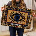 Evil eye doormat held indoors, showing the detailed blue, gold, red, and black artwork