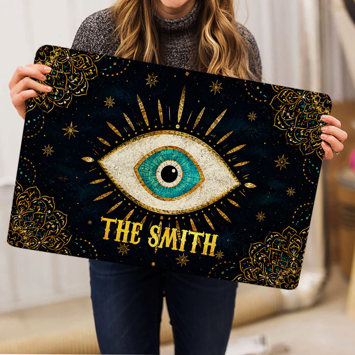 Evil eye doormat held indoors, showing its large turquoise eye and ornate celestial design