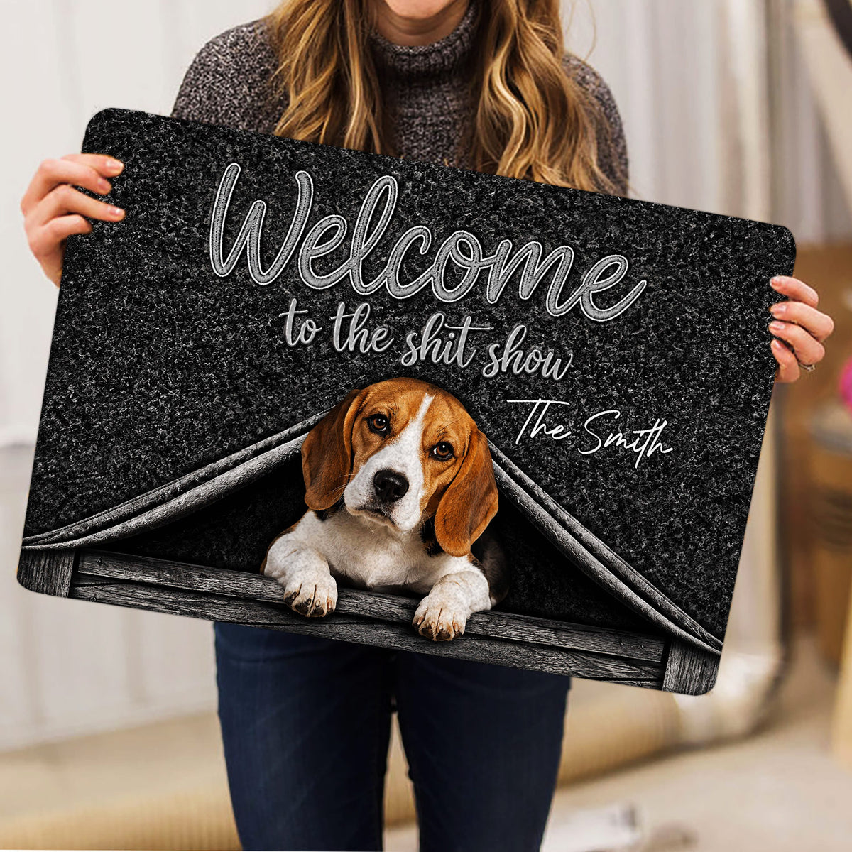 Person holding a black Beagle doormat featuring a playful welcome design and doghouse artwork