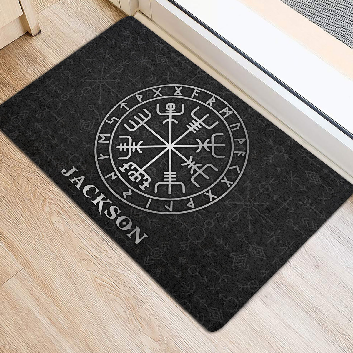 Black Viking entryway mat placed beside a door on light wood flooring