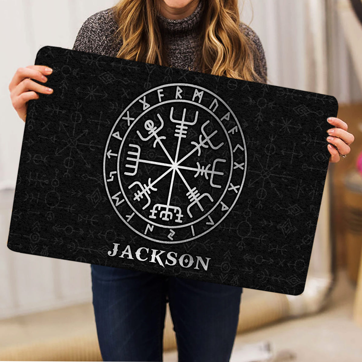 Person holding a black Viking doormat featuring a large circular Norse compass design