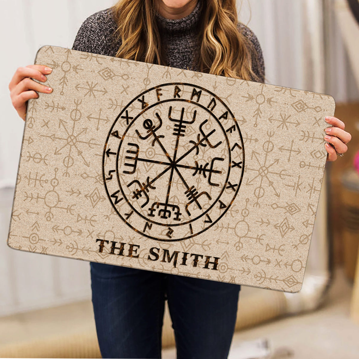 Person holding a Viking rune doormat featuring a central compass symbol and patterned Norse artwork