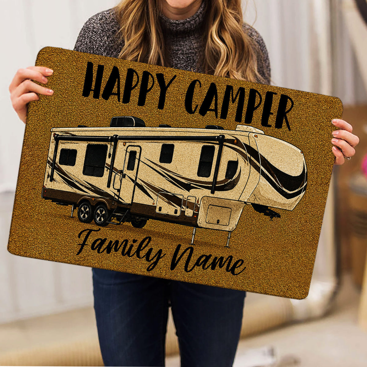 Person holding a golden camping doormat featuring a detailed recreational camper illustration