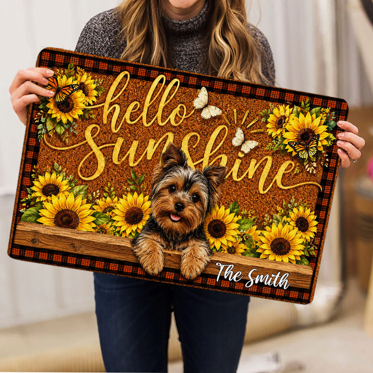 Person holding a Yorkie doormat featuring a smiling Yorkshire Terrier, sunflowers, butterflies, and welcoming script