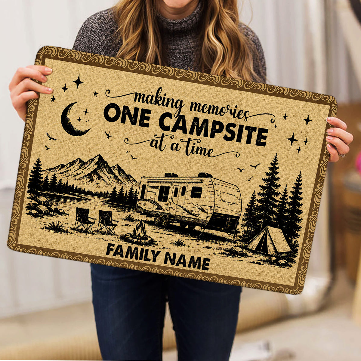 Camping doormat held indoors showing RV, tent, campfire, mountains and pine tree artwork