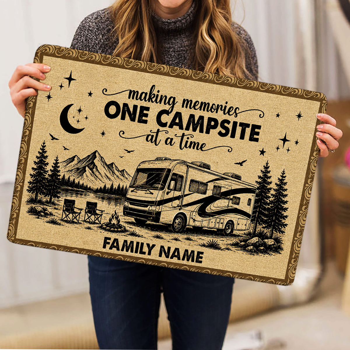 Camping doormat held indoors, displaying an RV by the mountains with pine trees, stars, and camp chairs
