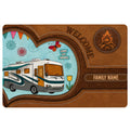Camping doormat featuring a motorhome, campfire emblem, colorful travel artwork, and rustic brown stitched-style borders