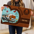 Camping-themed doormat held indoors, displaying a motorhome illustration, campfire emblem, and rustic entryway design