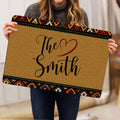Person holding a tan doormat with colorful geometric borders and heart-themed artwork