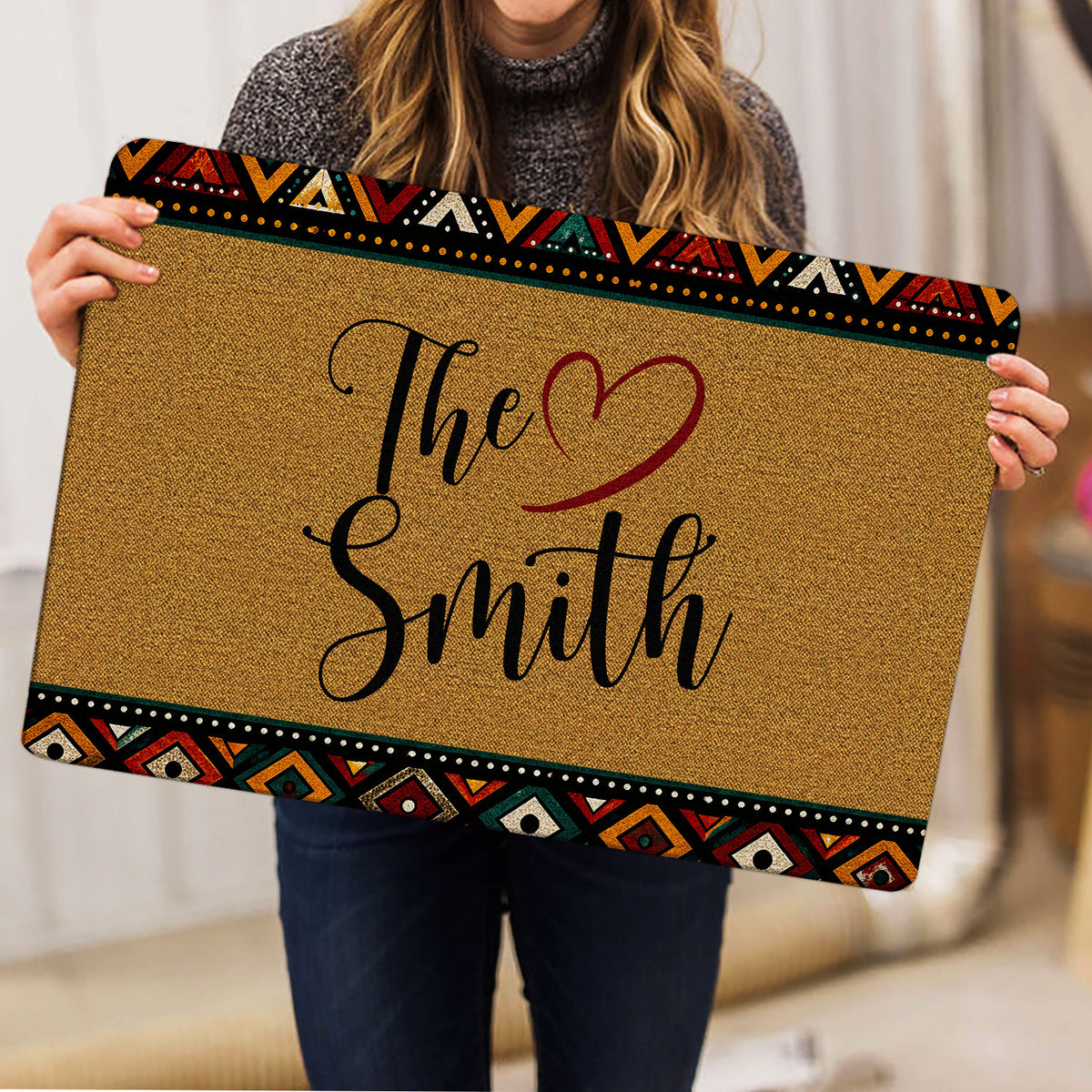 Person holding a tan doormat with colorful geometric borders and heart-themed artwork