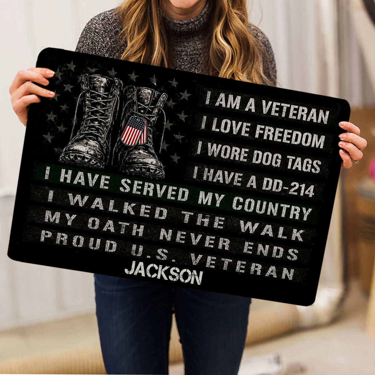 Person holding a black veteran doormat featuring military boots, dog tags, stars, and service-inspired artwork