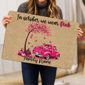 Woman holding a breast cancer awareness doormat featuring a pink ribbon tree, pumpkins, and pink truck