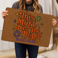 Person holding a colorful hippie doormat featuring flowers, stars, retro lettering, and peace-inspired artwork