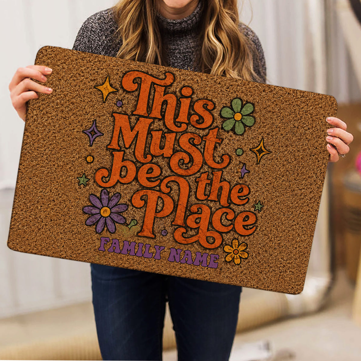 Person holding a colorful hippie doormat featuring flowers, stars, retro lettering, and peace-inspired artwork