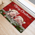 Festive pig doormat positioned at an indoor doorway with two Santa hat pigs, greenery, and ornaments