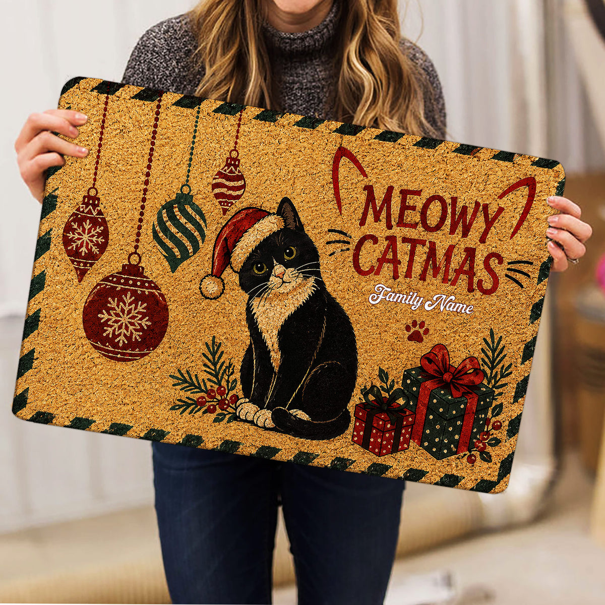 Person holding a Christmas tuxedo cat doormat featuring ornaments and wrapped gifts