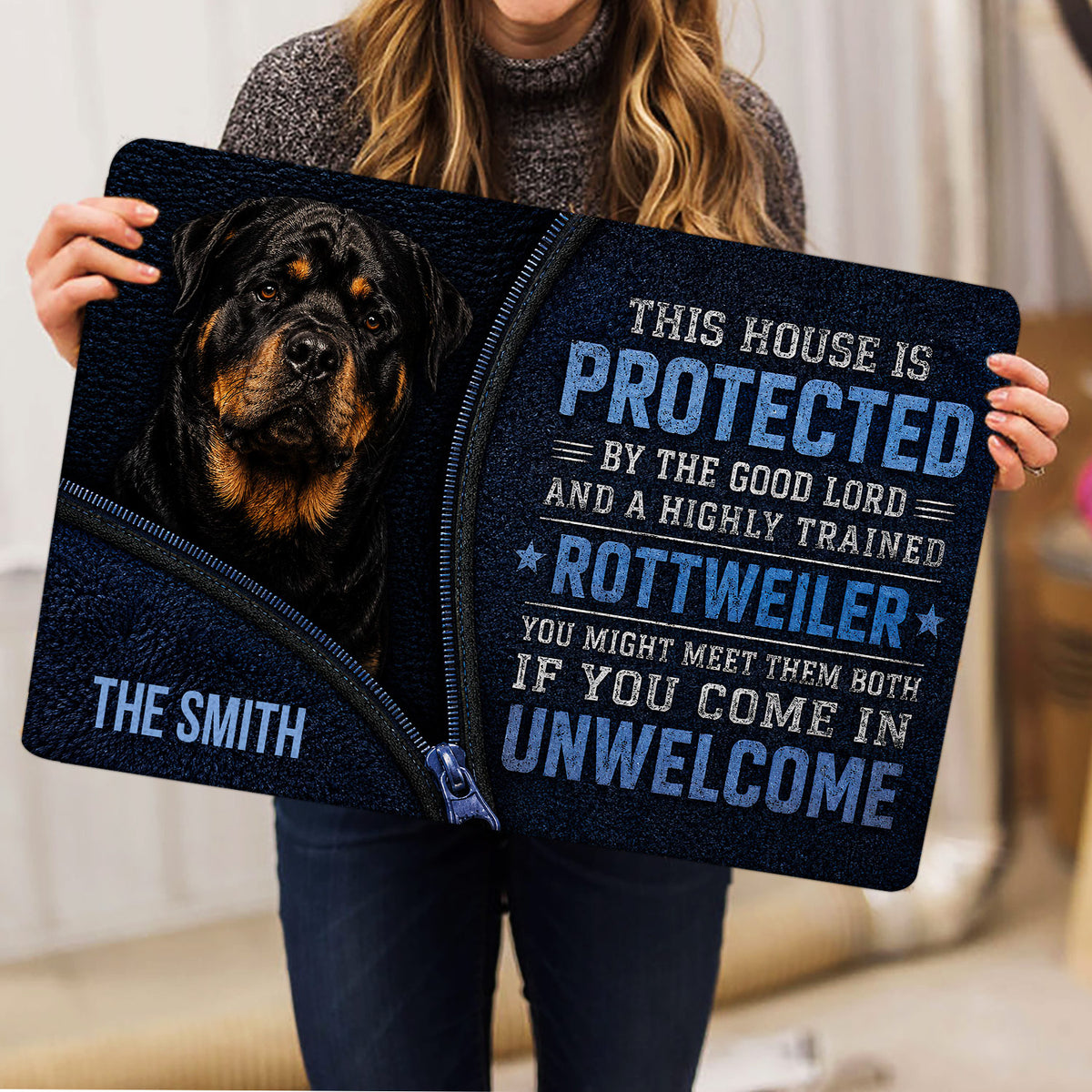 Person holding a Rottweiler doormat featuring a dog portrait and bold blue protective message