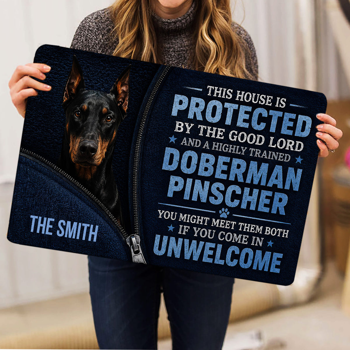 Person holding a Doberman Pinscher doormat with bold blue and black artwork