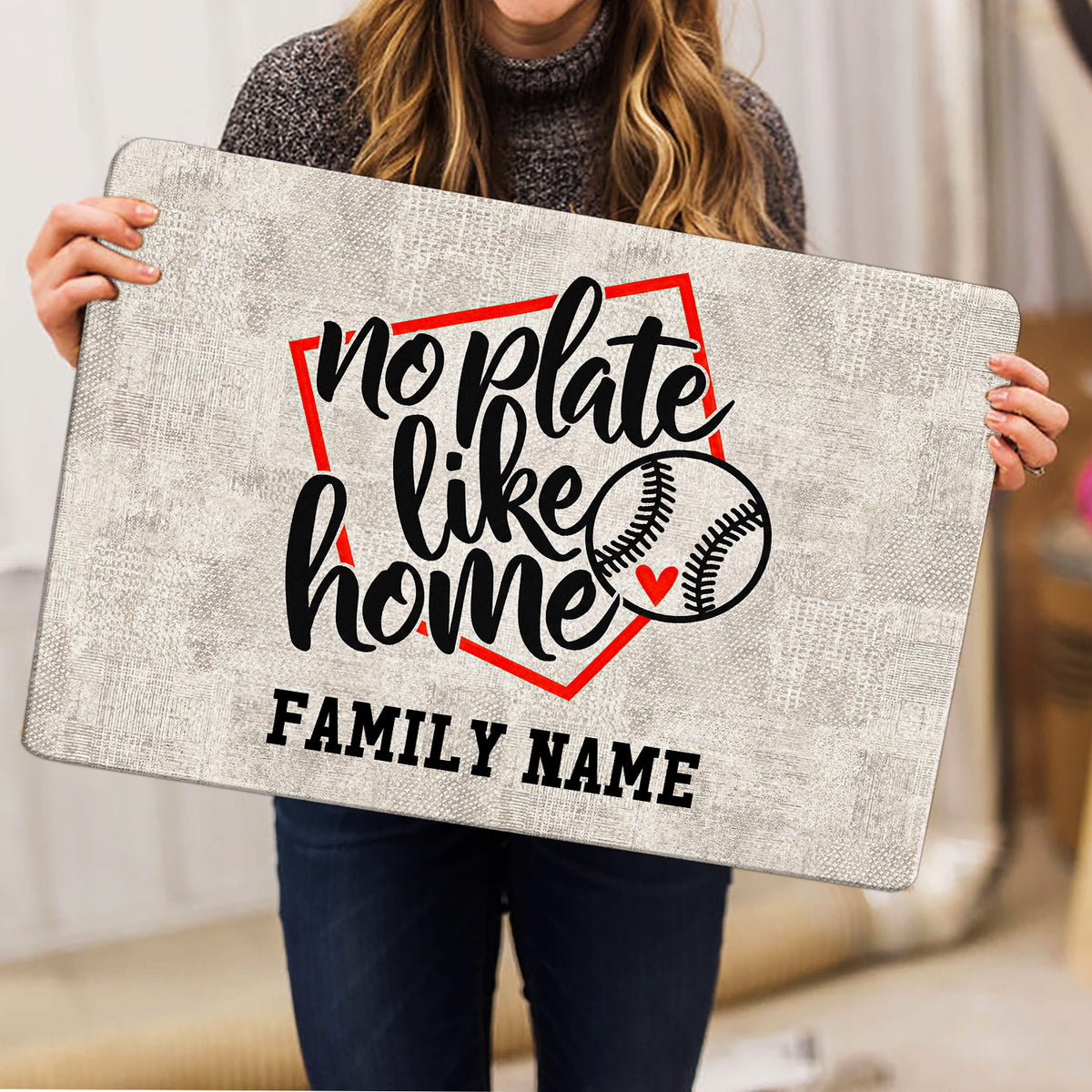 Baseball-themed doormat held indoors, showing bold script lettering, red accents, and baseball illustrations