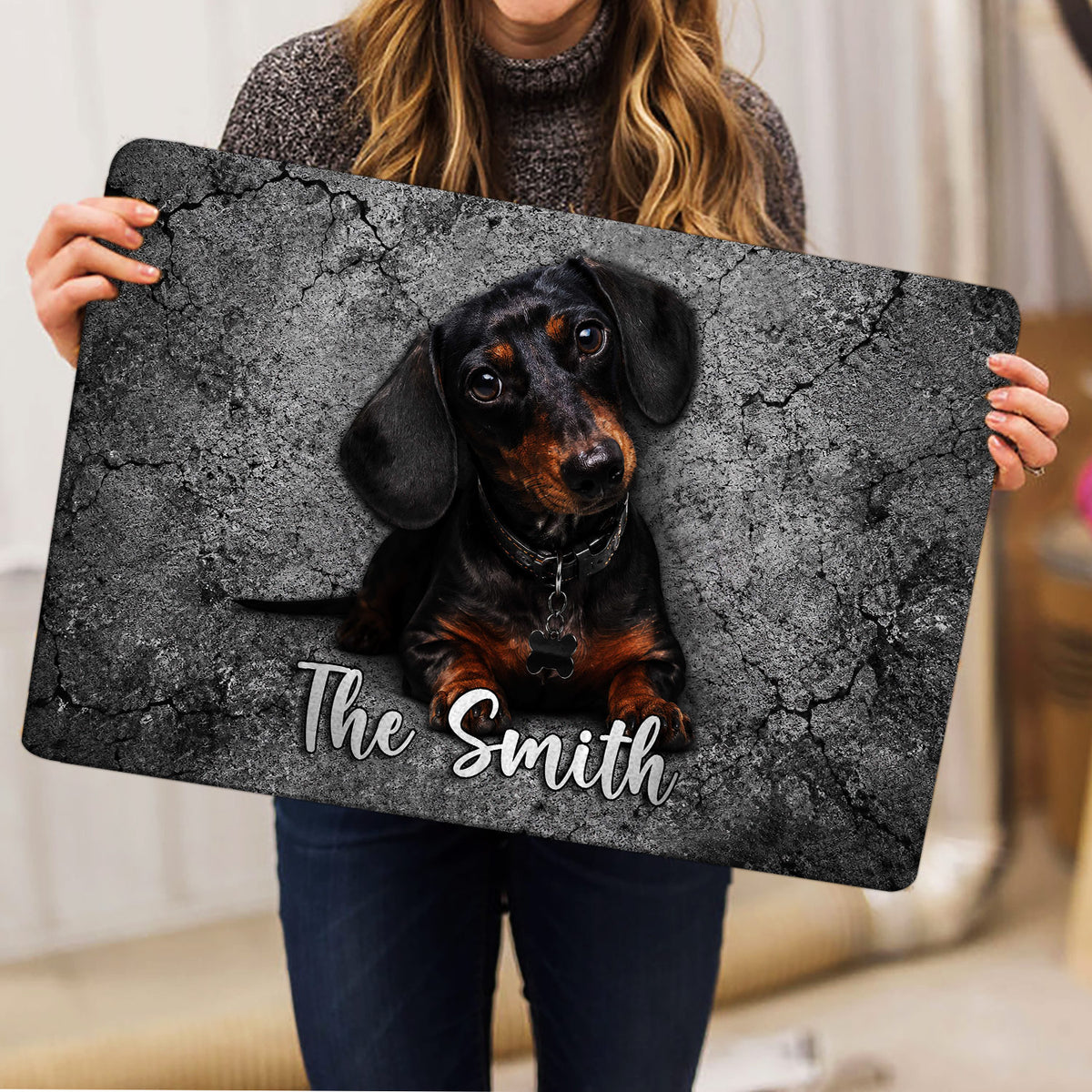 Person holding a dachshund doormat featuring a black and tan dog portrait on a gray background