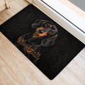 Black dachshund door mat positioned beside an interior doorway on light wood flooring