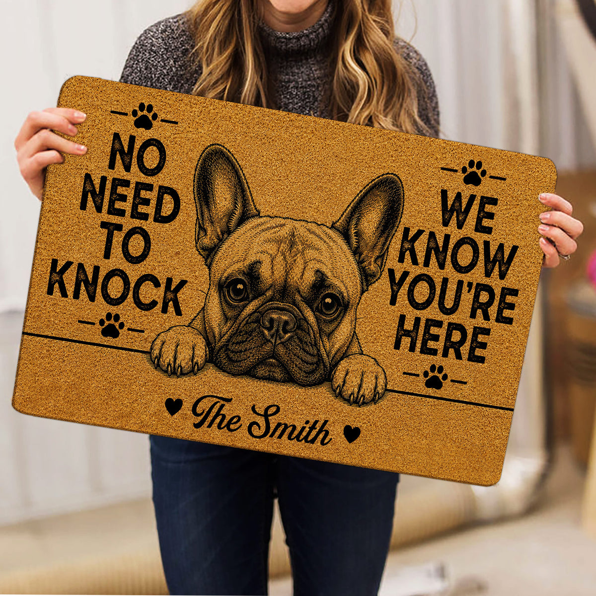 Person holding a tan French Bulldog doormat featuring a bold dog portrait, paw prints, hearts, and lettering