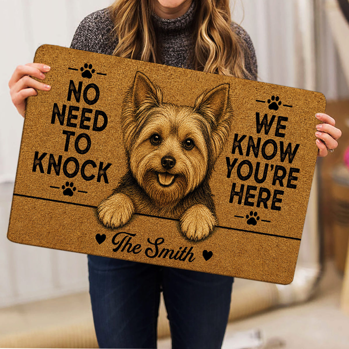 Person holding a tan Yorkie doormat featuring a playful Yorkshire Terrier illustration and paw prints