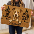 Person holding a pitbull doormat featuring a smiling dog portrait, paw prints, hearts, and bold black lettering