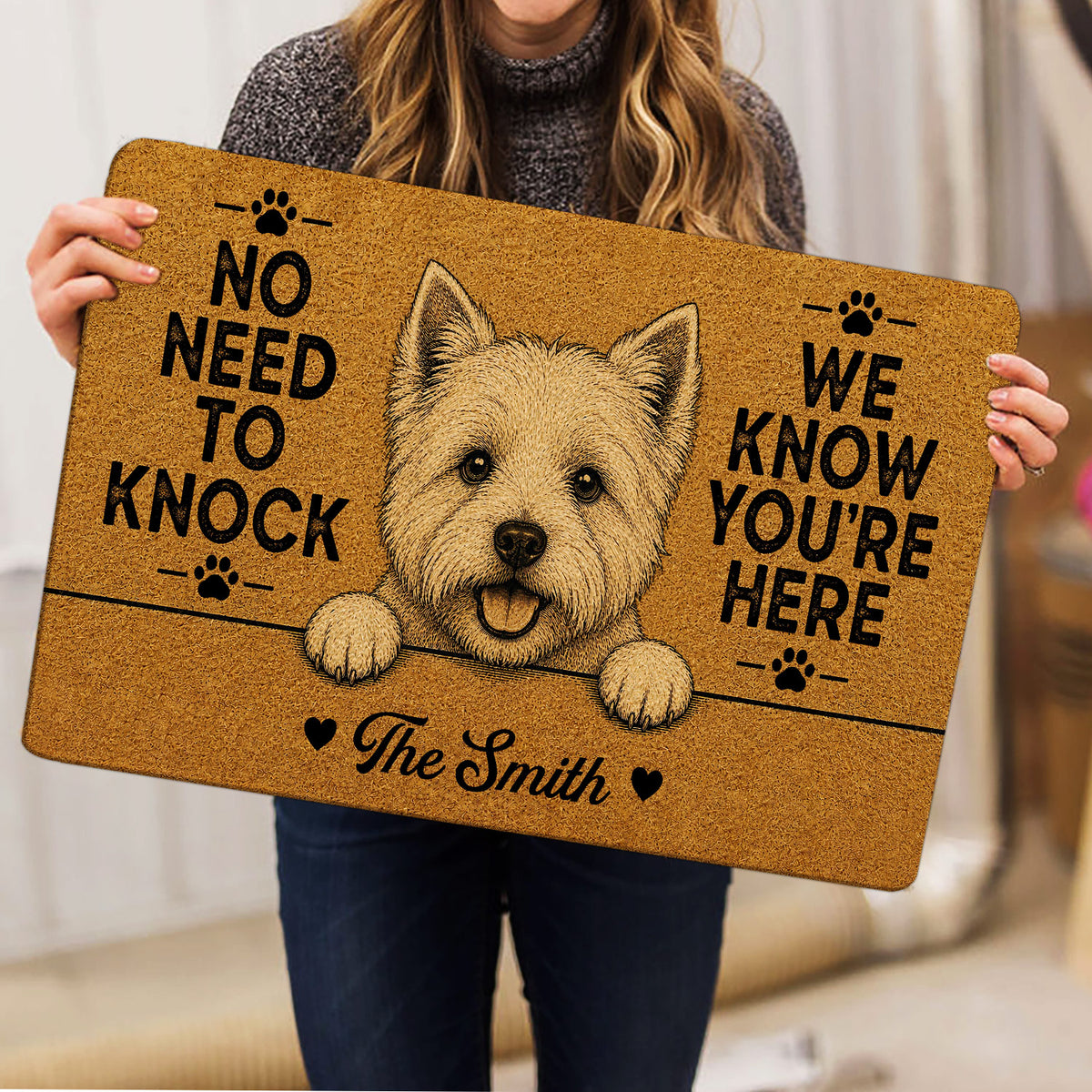 Person holding a Westie doormat featuring a terrier portrait, paw prints, and a welcoming entryway message