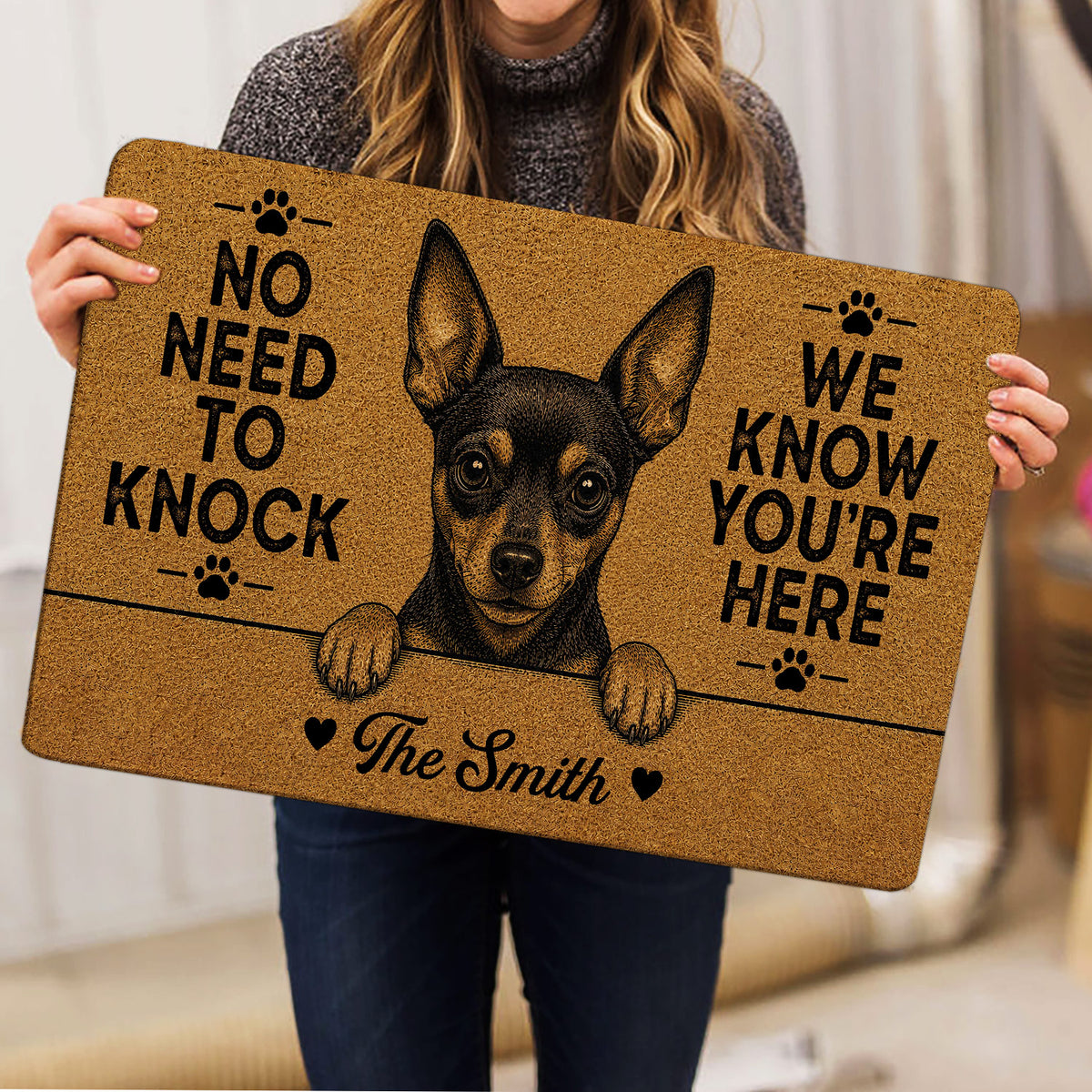 Person holding a Miniature Pinscher doormat with bold paw prints and warm brown artwork