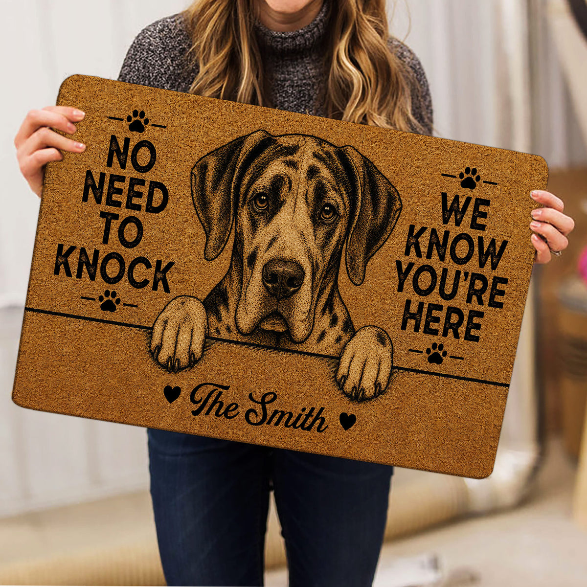 Person holding a brown Great Dane doormat with paw prints, hearts, and bold welcome lettering