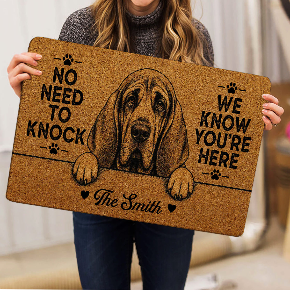 Person holding a tan bloodhound doormat featuring a detailed dog portrait and paw prints
