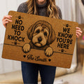 Person holding a tan Schnoodle doormat with dog artwork, paw prints and bold black lettering