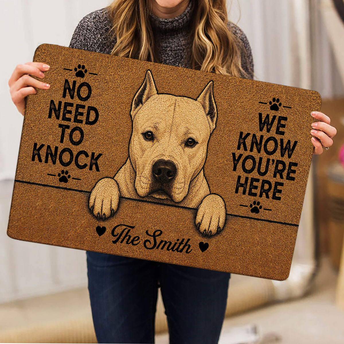 Dogo Argentino doormat held indoors, showing the white dog artwork, paw prints, and bold entryway message