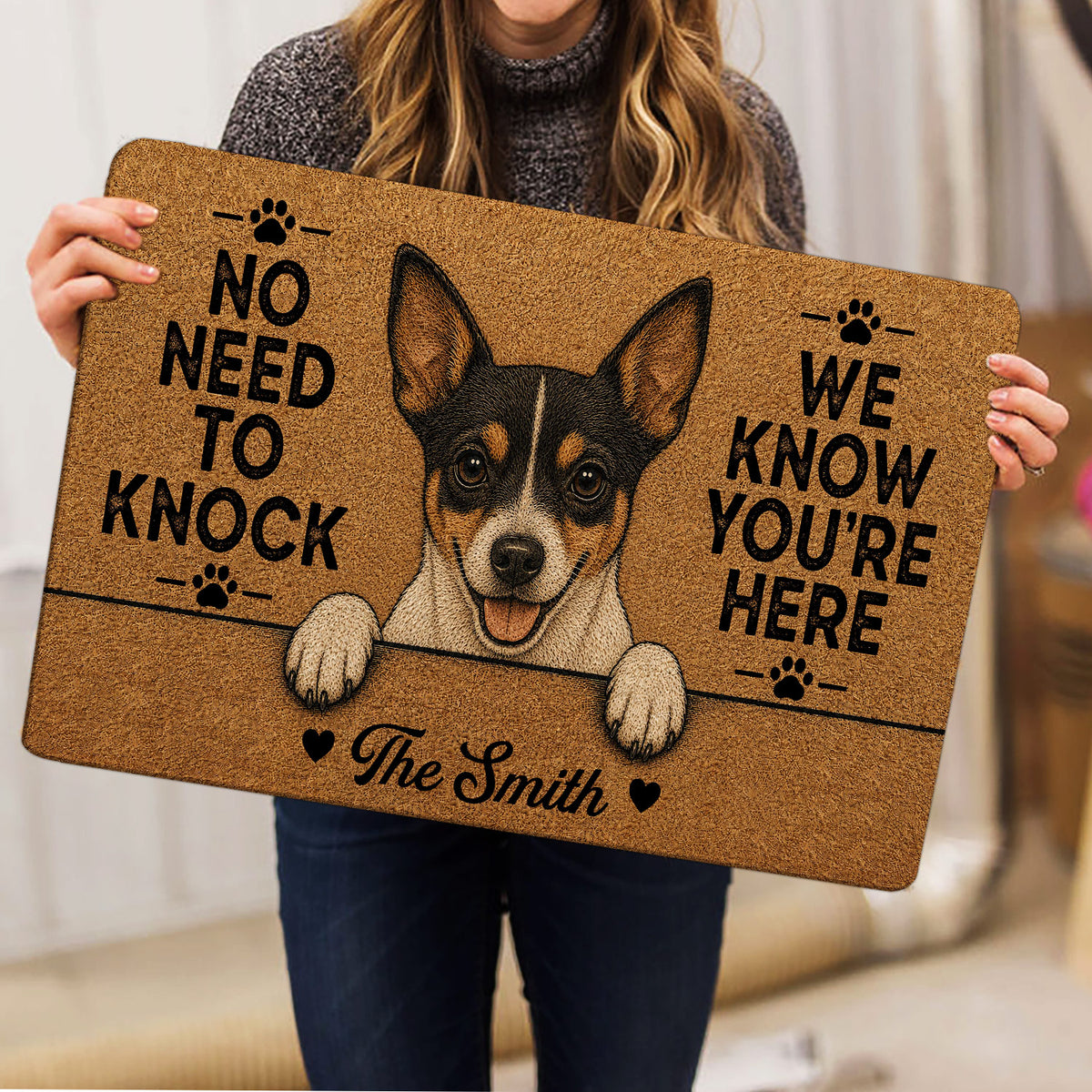 Person holding a tan Rat Terrier doormat with a playful dog portrait and paw print accents