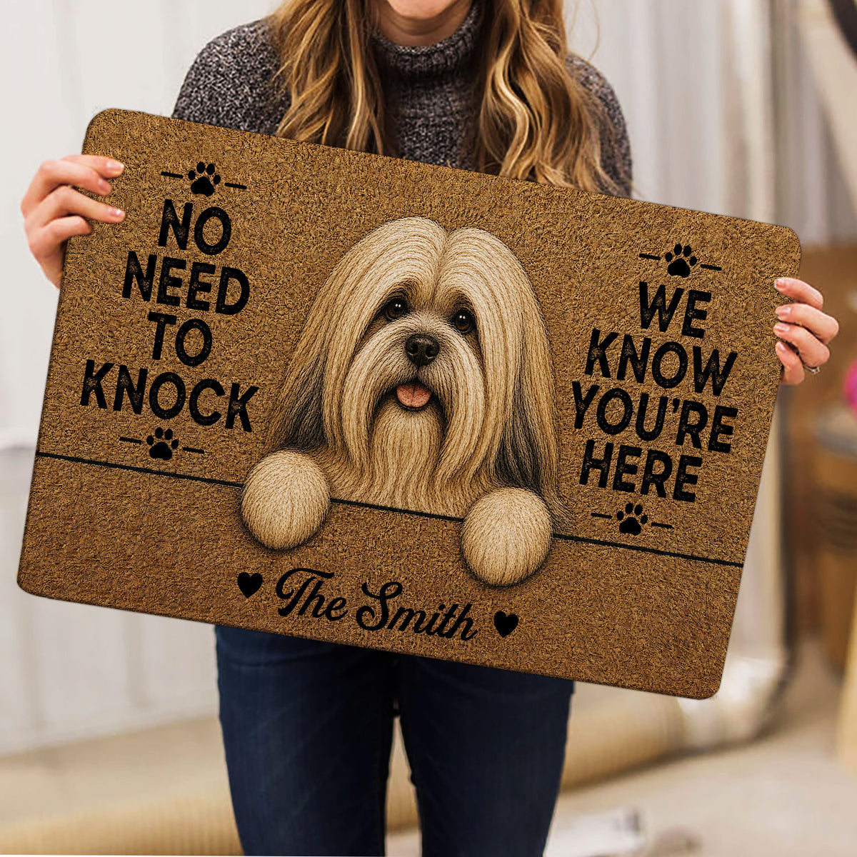 Lifestyle view of a person holding a Lhasa Apso doormat with a detailed dog portrait and paw print design
