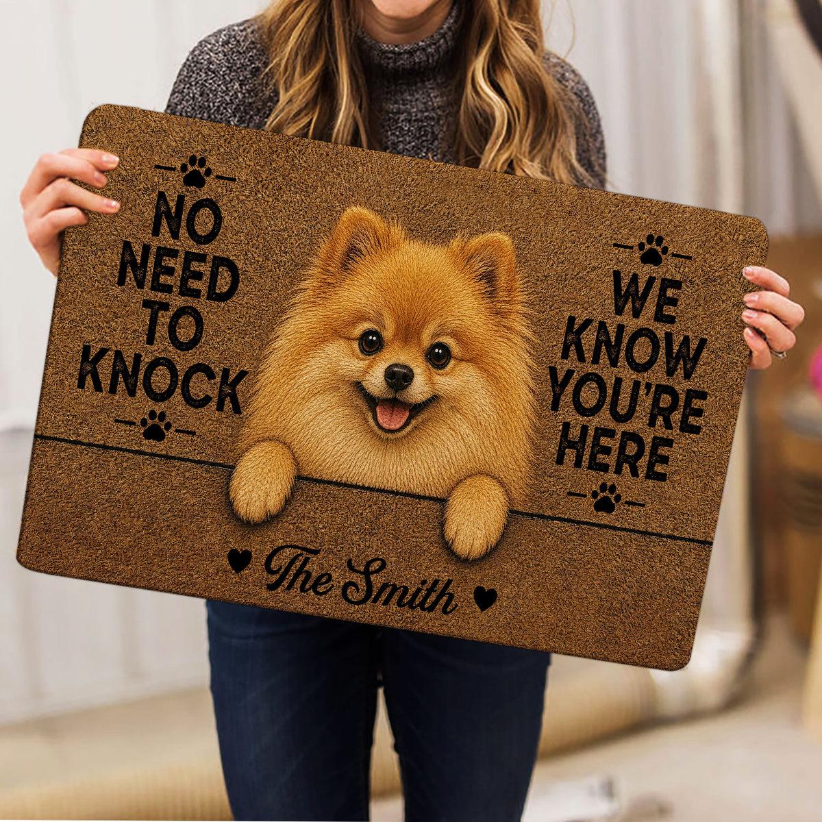 Person holding a Pomeranian doormat displaying a fluffy tan dog, paw prints, hearts, and welcoming lettering