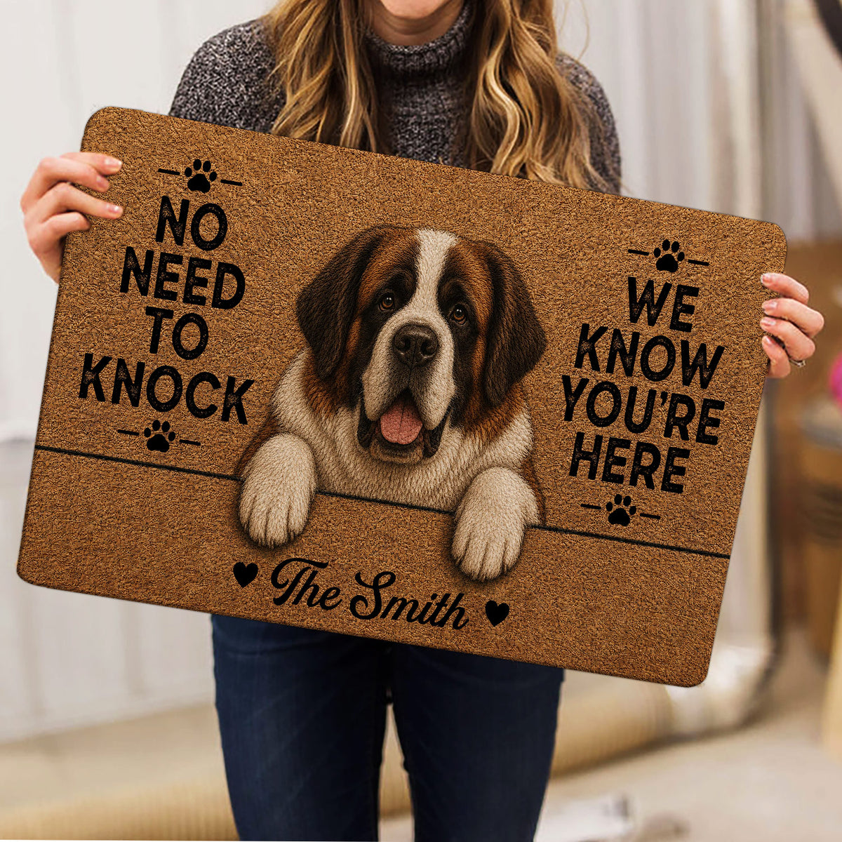 Saint Bernard doormat held indoors, showing the smiling dog portrait, paw prints, and bold lettering