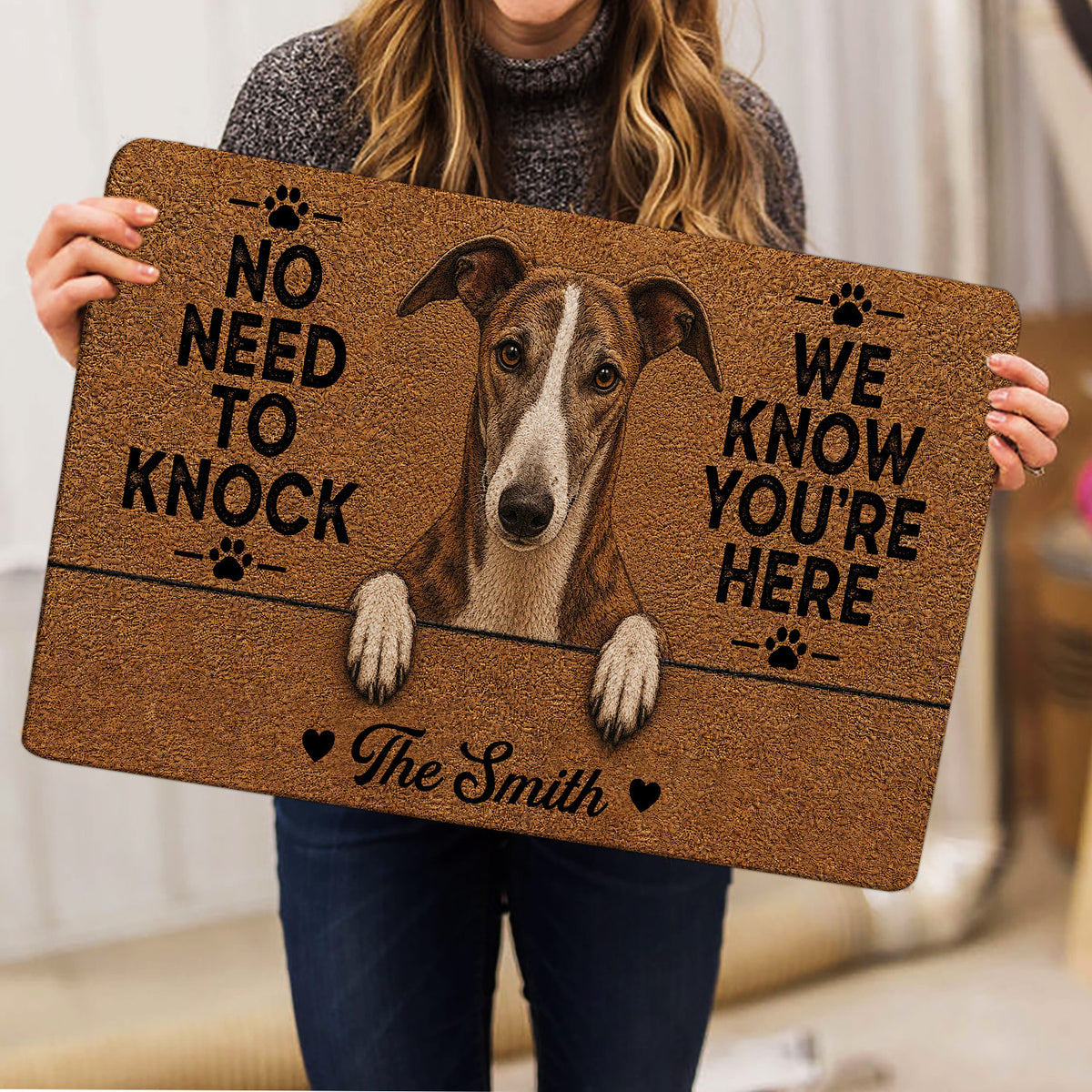 Person holding a greyhound doormat with a realistic dog portrait and bold black lettering